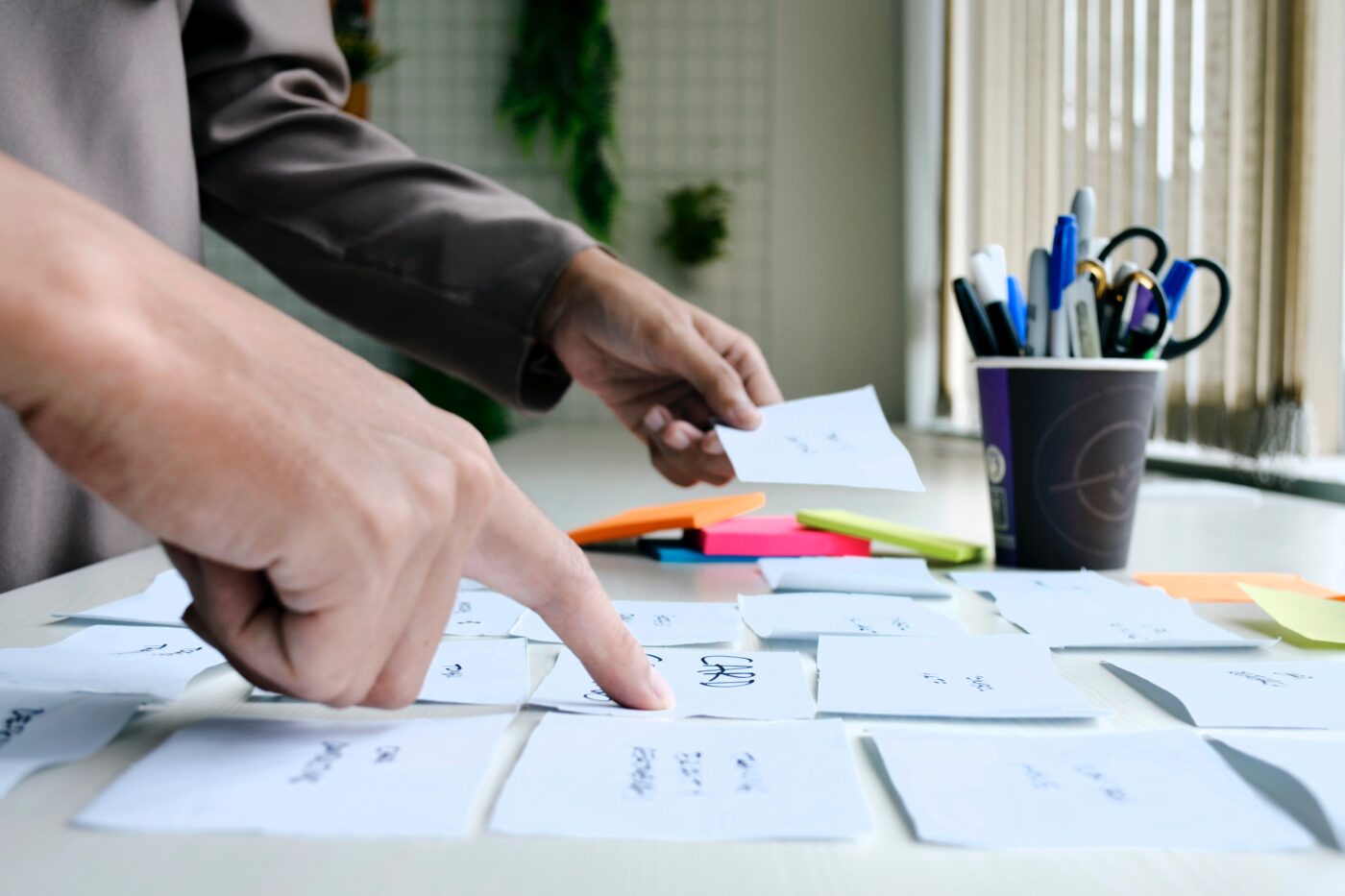 To personer står ved et bord fyldt med håndskrevne sedler og farvede post-its.